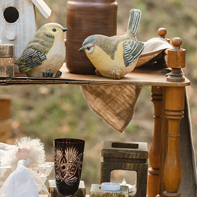 two decorative bird figurines on a wooden shelf with pottery and a glass cup in a vintage setting showcasing five unique objects