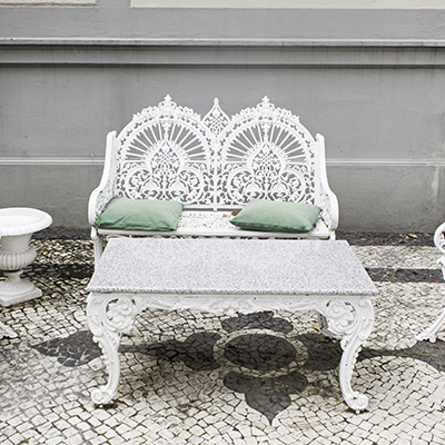 ornate white metal bench with two green cushions and matching table on patterned stone floor