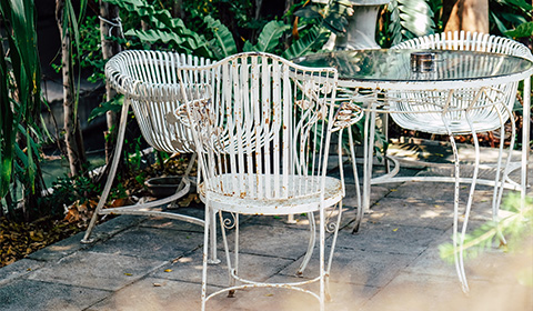 white iron patio furniture with eight legs and a glass top in a garden setting