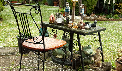 a black and orange chair beside a decorative table filled with various garden ornaments and figurines on a grassy area with fallen petals or snowflakes showcasing a charming outdoor decor setting for relaxation and enjoyment