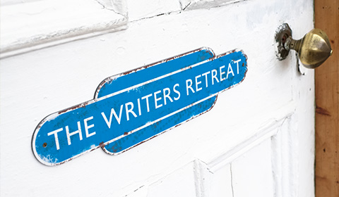 A close-up of a blue sign on a white door that reads The Writers Retreat suggesting a quiet place for inspiration and creativity for writers.
