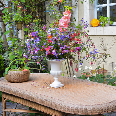 vibrant flower arrangement in white vase on rustic wicker table surrounded by blooming garden scene with colorful flowers suggesting a celebration of nature and nine floral varieties