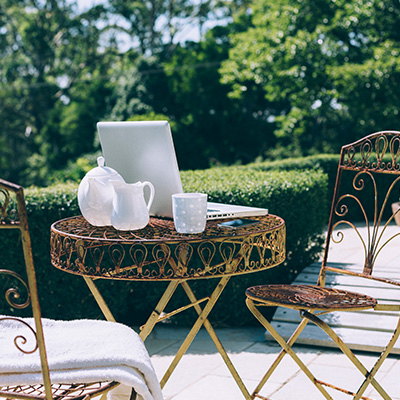 cozy outdoor workspace with a laptop teapot and cup on a round metal table in a green garden setting perfect for relaxing or working six days a week
